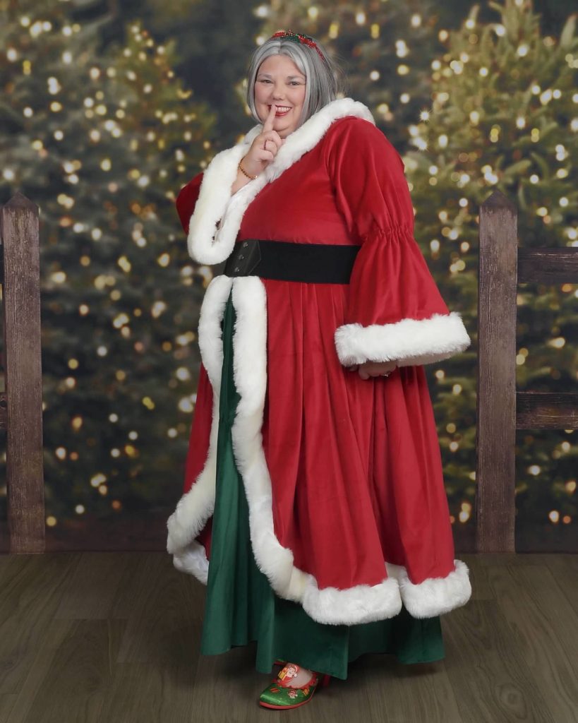 Mrs. Claus in a red fur-trimmed coat over a green dress