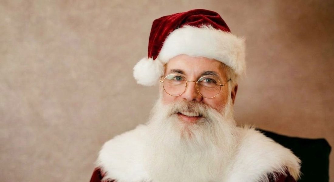Santa Rob Kowalski in a red velvet Santa suit and hat with round gold glasses